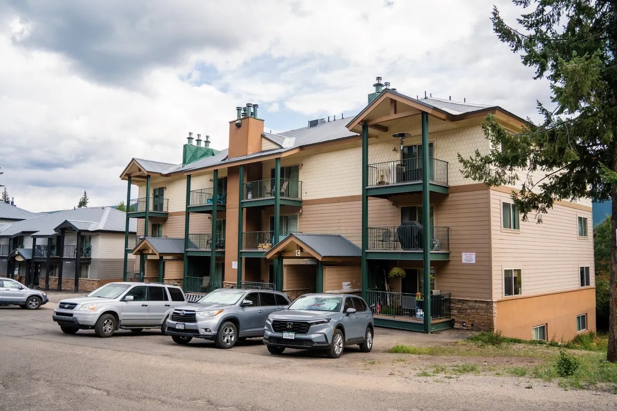 This exterior image showcases a multi-story townhome building with balconies adorned with plants and parked cars nearby. The communal outdoor area is inviting, and the balconies suggest places for private relaxation while still connecting residents to the outdoors. There is a warm, welcoming atmosphere, with the potential for sunset views from the balconies.