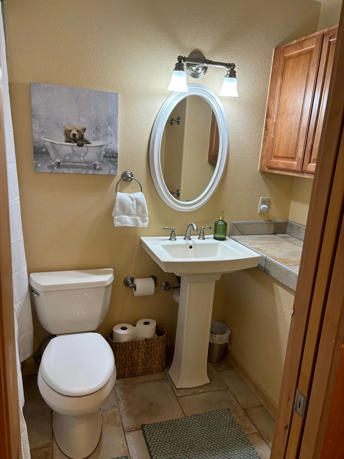 This image shows a cheerful bathroom scene featuring whimsical bear artwork above a well-lit sink, a large mirror, and modern light fixtures. The space is bright and inviting, emphasizing personal grooming and relaxation routines. The overall mood is light-hearted and rejuvenating.
