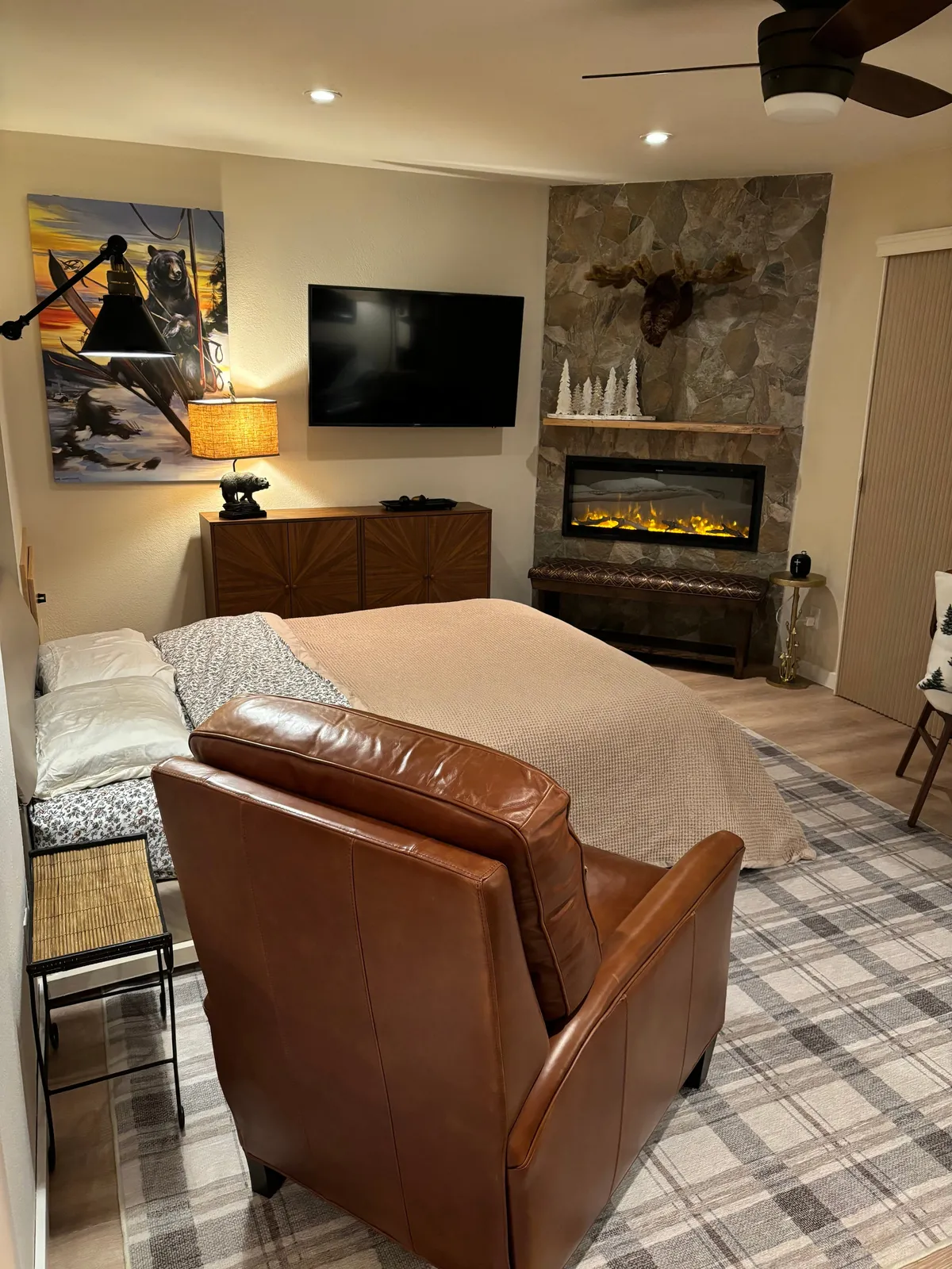 This image centers on the sleeping area, featuring a plush bed positioned near a fireplace, a comfortable leather chair, and cozy artwork. The arrangement exudes warmth and provides a home-like, intimate feel—the perfect space to unwind after a day outdoors.