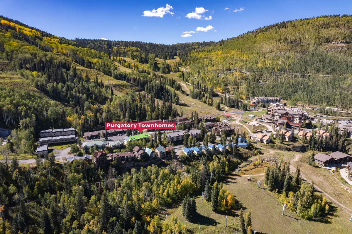 A sweeping exterior view of Purgatory Townhomes, with lush green forest, mountain slopes, and visible ski and hiking trails cutting through the landscape. This scene highlights both adventure and a peaceful retreat in nature.