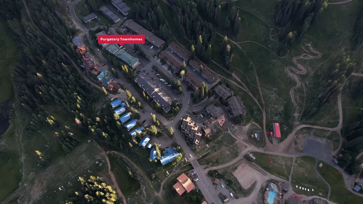 This image captures the Purgatory Townhomes nestled among tall pine trees, surrounded by open green areas and with the dramatic backdrop of ski slopes and mountains. The setting exudes a sense of adventure and tranquility, with easy access to hiking trails and nature just beyond the doorstep.