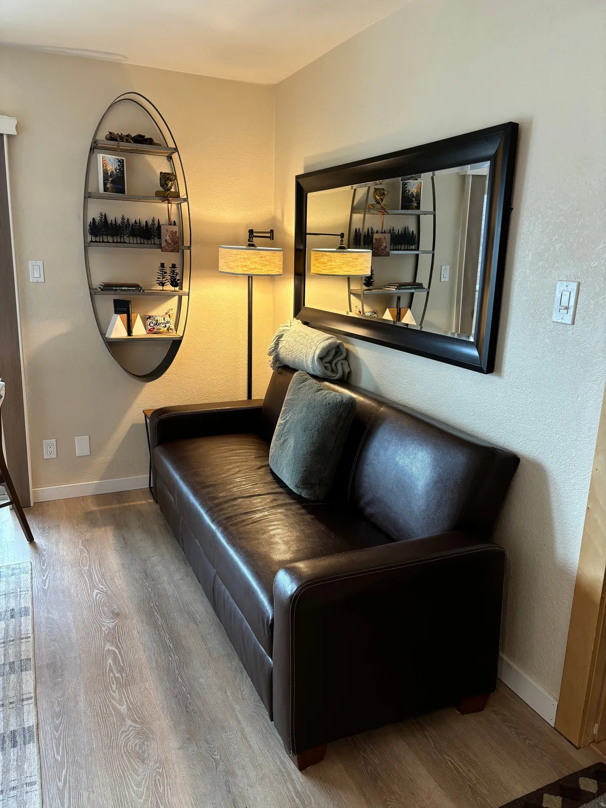 A comfortable living space featuring a plush sofa, a bookshelf, a mirror, and a softly lit lamp, creating a homely atmosphere that encourages relaxation and socializing.